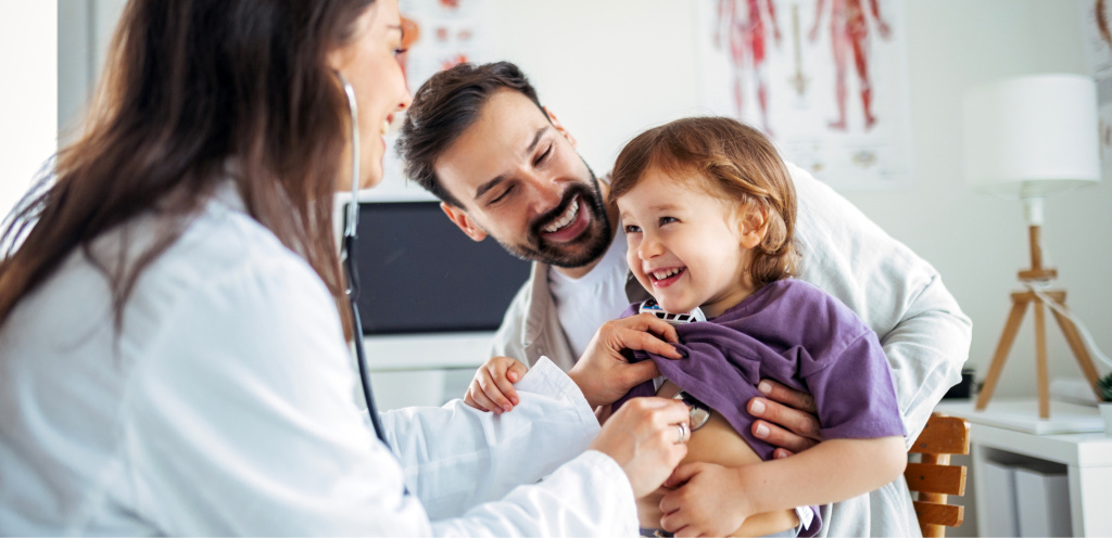 Педиатр проводит осмотр двухлетнего ребёнка с родителями — диспансеризация в 2 года